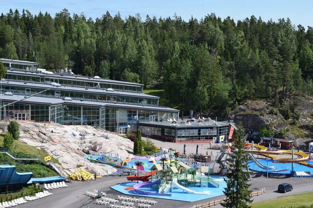 Water park complex with colorful slides and pools beside a rocky slope and dense forest.